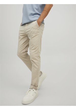 Chinos beiges avec poches latérales, coupe fuselée et détails cousus. Assortis à des baskets blanches montantes. Tissu simple et texturé.