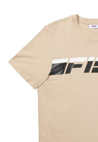 T-shirt beige à manches courtes avec un logo FILA audacieux en noir, blanc et beige sur la poitrine et un col rond.