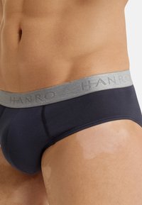 Marinefarbene Baumwollunterhosen mit einem grauen elastischen Bund, der den Markennamen "HANRO" in einem erhabenen Design zeigt. Glatte Textur und enganliegende Passform.