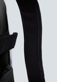 Spallacci di uno zaino nero con un design imbottito e una rete sovrapposta per la traspirabilità. Bordo liscio e cuciture rinforzate visibili.