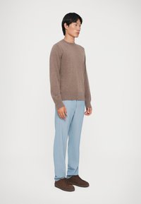Brun sweater med rund hals, lyseblå stribede bukser og brune sneakers. Outfitet har subtile teksturer og en moderne pasform.