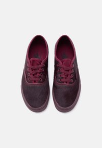 Ζεύγος μπορντό χαμηλά παπούτσια με κορδόνια, με υφασμάτινο επάνω μέρος με υφή και λαστιχένιες σόλες, εμφανιζόμενα από πάνω σε λευκό φόντο.