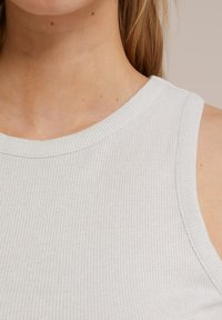 Ljust grå ribbad linne gjort av stretchigt material, med en vid halsringning och utan ärmar. Subtil textur ger dimension.
