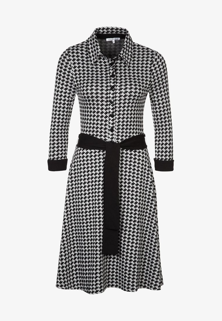 Robe chemise à manches longues avec motif pied-de-poule noir et blanc, poignets noirs et ceinture noire nouée à la taille.