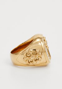 Gouden ring met een driehoekige vorm, voorzien van een bloemmotief aan de voorkant en diamanten accenten aan één zijde. Gladde, glanzende textuur.