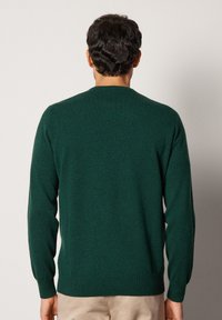 Mörkgrön ulltröja med rund halsringning, långa ärmar och ribbade cuffs och nederkant. Slät textur, odekorerad bakvy.