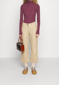 Lichtpaarse coltrui, beige wijde broek, bruine schoenen en een kleine handtas van zwart en bruin gestructureerd materiaal.