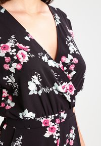Robe noire à fleurs avec des fleurs roses et blanches. Décolleté en V, taille froncée et texture de tissu douce. Silhouette fluide.