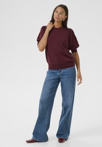 Burgundy stickad tröja med puffärmar, kombinerad med vida jeanstajl. Mjuk textur och avslappnad passform, vilket framhäver en avslappnad silhuett.