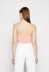 Camisola justa cor-de-rosa claro com alças finas ajustáveis, apresentando um painel franzido nas costas. Combinada com calças de ganga brancas de cintura alta.