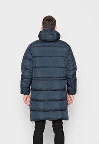 Mörkblå vadderad jacka med hög krage och elastiska ärmslut, med horisontella kviltade sektioner och en ledig passform.