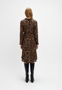 Sukienka w wzór lamparta z długimi rękawami, z wciągniętą talią i długością do kolan, połączona z czarnymi kozakami do kolan. Gładka tekstura i zwiewny krój.