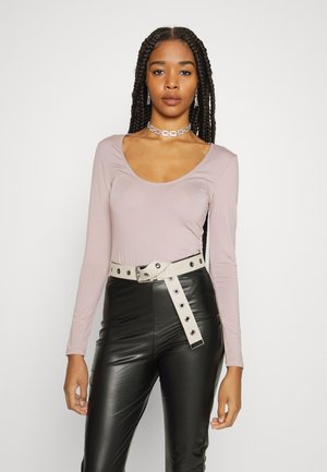Camisola de mangas compridas e decote em coração em tecido rosa claro, combinada com calças pretas de imitação de pele de cintura alta e um cinto bege com detalhes metálicos.