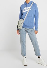 Blå hoodie med en stor vit Nike-logotyp, i kombination med ljus tvättade jeans och vita sneakers. Inkluderar en liten grå axelväska.