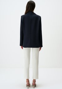 Blazer navy con vestibilità su misura, maniche lunghe, rever a lobature e schiena dritta, abbinato a pantaloni bianchi alla caviglia e tacchi a strappi.