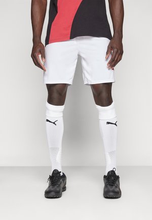 Hvide sportsshorts parret med sorte atletiske sko, hvide sokker med et sort logo og en sort-rød farveblokkeret skjorte.