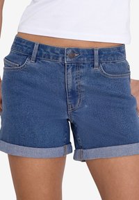 Denim šorti vidēji zilā krāsā, ar klasisku piecu kabatu dizainu, ar apgrieztām malām un ar rāvējslēdzēju, kas aizveras ar pogu.