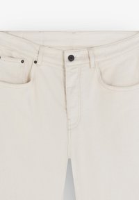 Bílé džíny z denimu se standardním pasem, předními kapsami a zipem. Mají černý kovový knoflík a odolné švy.