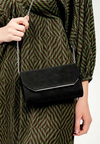 Fekete műbőr clutch táska mágneses záródással, ezüst láncos pánttal és letisztult, minimalista dizájnnal.