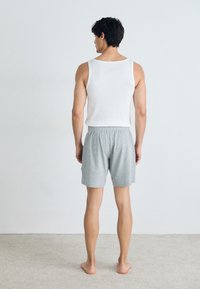 Hvit tanktopp og lysegrå shorts. Tanktoppen har brede stropper, mens shortsen har elastisk midje og klassisk snitt.