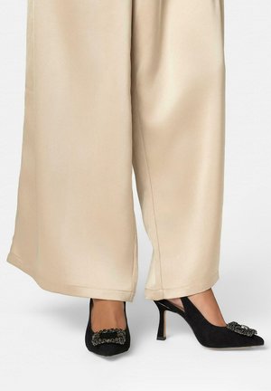 Pantalones beige de pierna ancha con zapatos negros de tacón alto que tienen hebillas cuadradas decorativas en la parte delantera.