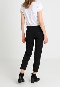 Pantalons noirs fuselés avec une taille mi-haute et deux poches arrière, associés à un t-shirt blanc ajusté et des bottines.