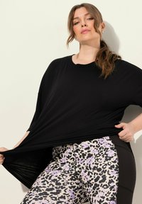 T-shirt nera oversize con maniche corte, abbinata a leggings con stampa leopardata lilla e nera e tasche sui fianchi.