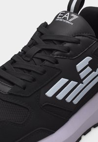 Μαύρο αθλητικό παπούτσι με μαύρα κορδόνια, λευκό λογότυπο EA7 Emporio Armani στη γλώσσα και λευκές σχηματοποιημένες ρίγες στο πλάι.