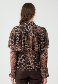 Blouse en imprimé léopard avec des détails de volants superposés, des manches longues et un col rond. Palette de couleurs riches en marron et noir, texture soyeuse.