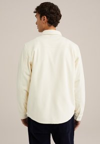 Cream-colored fleece shirt with long sleeves, buttoned cuffs, and a classic collar. Smooth texture and rounded hemline.