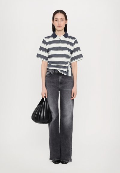 Stripet polotrop i marineblå og hvit, kombinert med høyt liv grå jeans. Holder en svart, plisséveske. Enkel, klassisk silhuett.