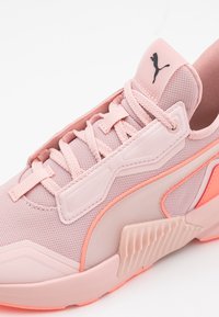 Světlounce růžová sportovní bota s horní částí z mesh materiálu a gumovými prvky. Obsahuje texturované překryvy a kontrastní oranžový detail na boku.