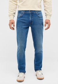 Blå denimjeans med rak passform, medelhögt midja, femficksdesign och ljus förstärkning. Matchas med krämfärgade sneakers.