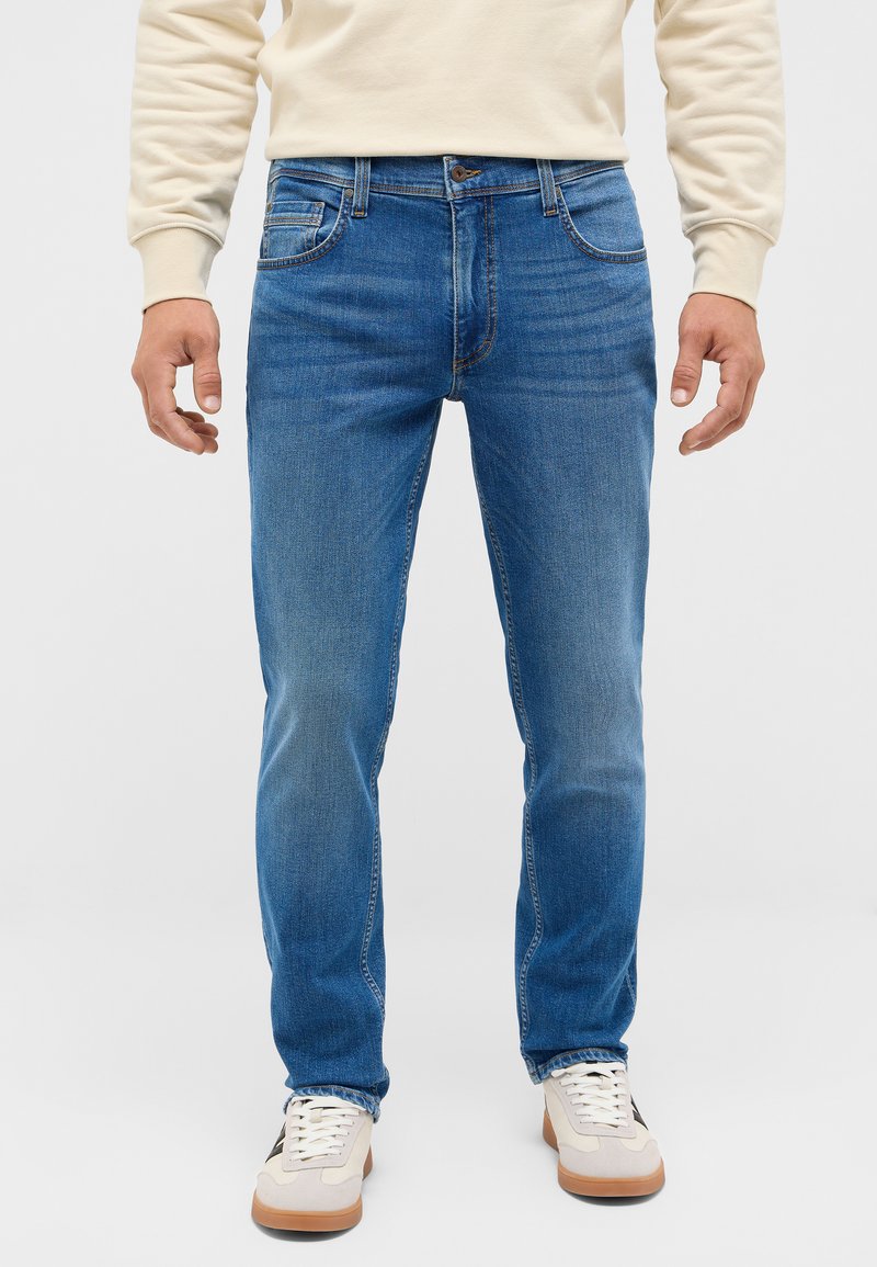 Blå denimjeans med rak passform, medelhögt midja, femficksdesign och ljus förstärkning. Matchas med krämfärgade sneakers.