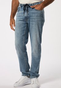 Pantalones de mezclilla azul claro con un corte relajado, cinturilla elástica y cordón. Combinados con zapatillas deportivas blancas y con detalles de costura visibles.