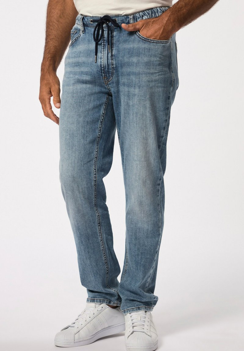 Pantalones de mezclilla azul claro con un corte relajado, cinturilla elástica y cordón. Combinados con zapatillas deportivas blancas y con detalles de costura visibles.