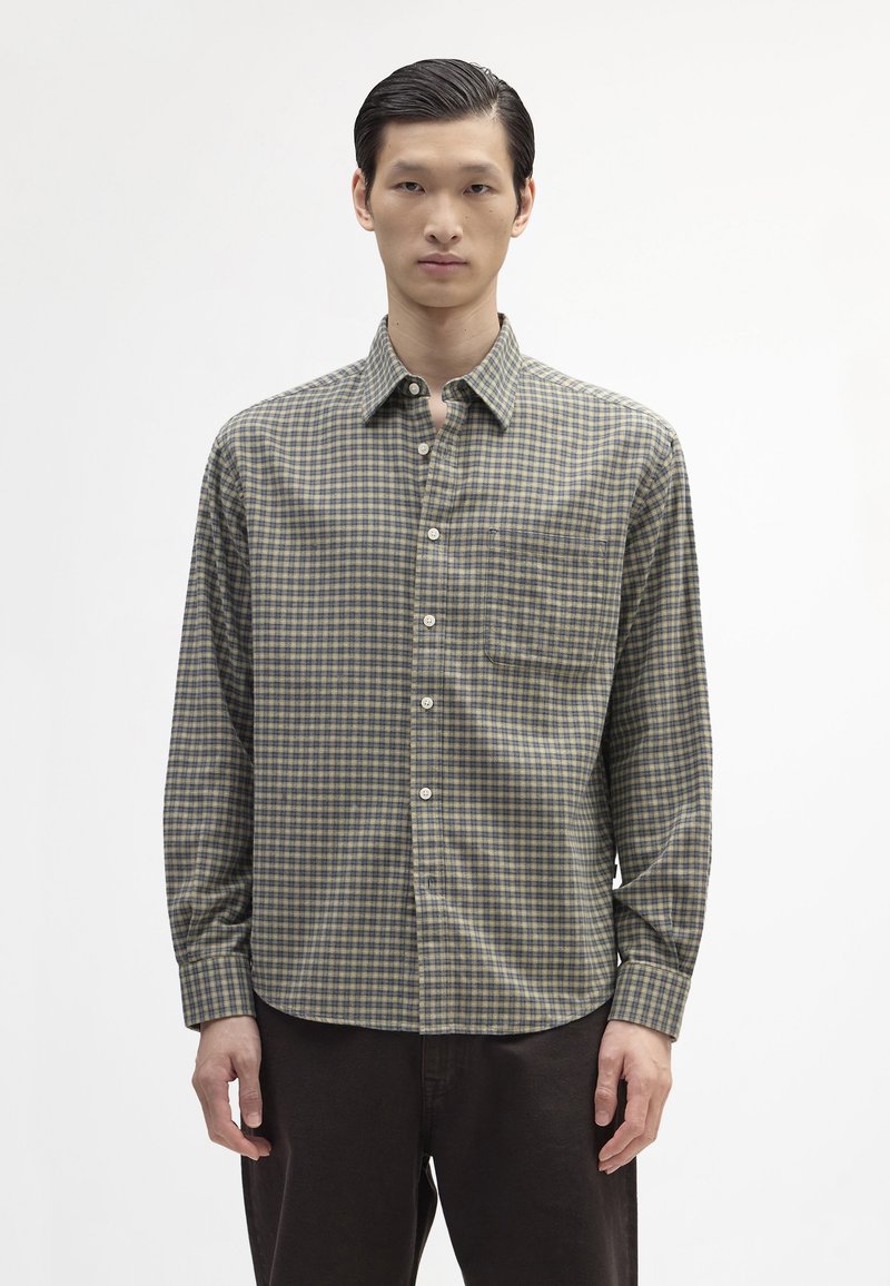 Grøn- og beige-ternet skjorte med krave, lange ærmer og en brystlomme. stoffet ser let og struktureret ud.