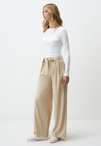 Beige wijde broek met een strik taille, gemaakt van een gladde stof. Gecombineerd met een aansluitend wit langslavend top en witte sneakers.