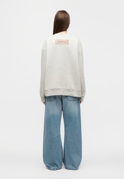 Felpa grigio chiaro con spalle scese, orlo a costine e un'etichetta sul retro. Abbinata a jeans di denim blu oversize con tasche.