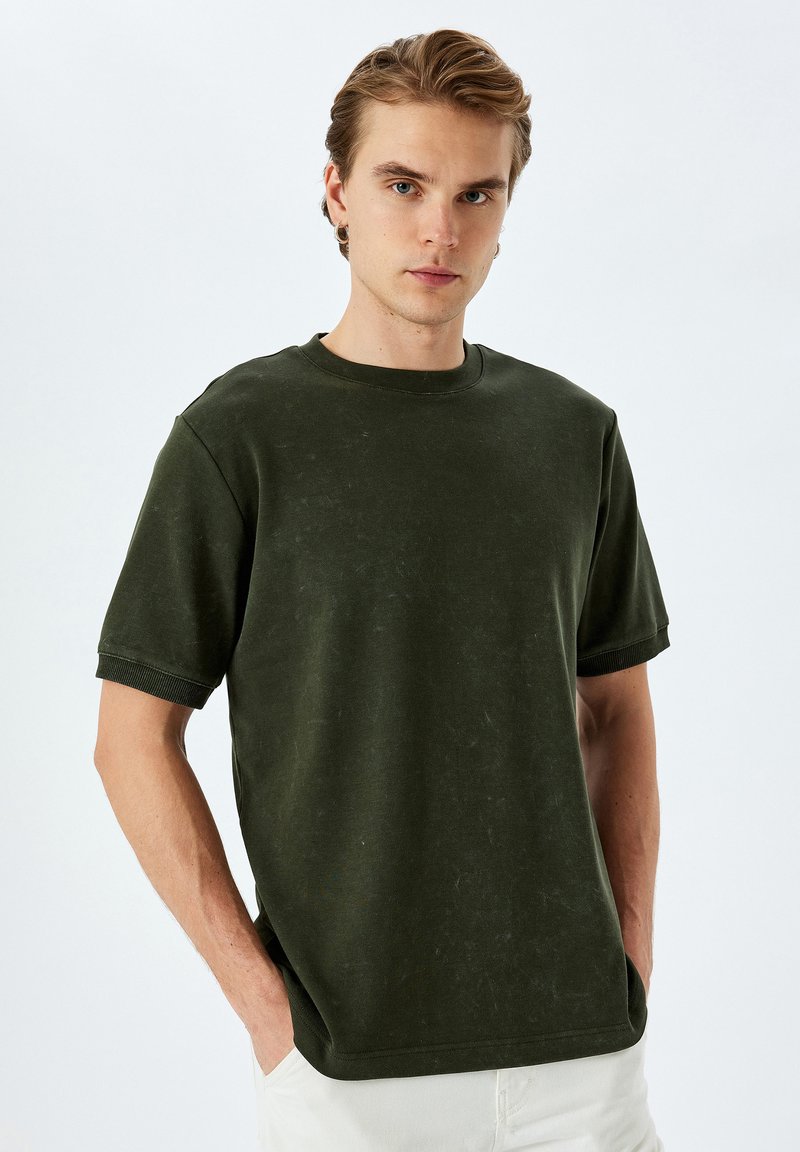 Mörkgrön t-shirt med korta ärmar och rund halsringning, med en avslappnad passform och en distinkt texturerad yta. Lättsam stil med ribbade detaljer vid ärmarna.