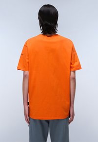 Orange bomulds T-shirt med korte ærmer og rund hals. Ensfarvet design med løs pasform. Synlige sømme ved kanten.