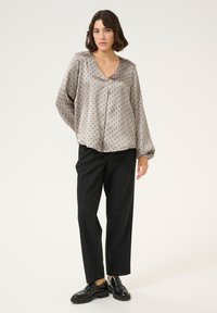 Grey polka dot blouse with balloon sleeves, V-neckline, and smooth fabric, paired with black tailored trousers and black shoes.