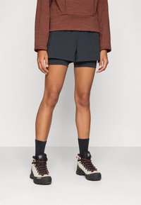 Dark gray shorts paired with a rust-colored oversized sweatshirt, complemented by beige hiking boots with red accents and dark socks.