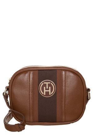 Brun læder crossbody taske med sort lodret stribe og rundt metal logoemblem i midten, med justerbar rem.