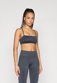 Γκρι αθλητικό σουτιέν με λεπτές τιράντες και τετράγωνη λαιμόκοψη, συνδυασμένο με ψηλόμεσα κολάν. Το υλικό φαίνεται μαλακό με υφή.