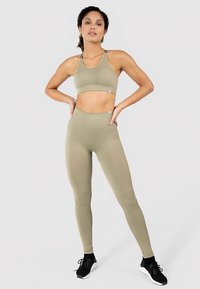 Khaki sportoutfit bestaande uit een cropped sportbeha met een geribbelde textuur en een legging met hoge taille, beide gemaakt van een glad, rekbaar materiaal.