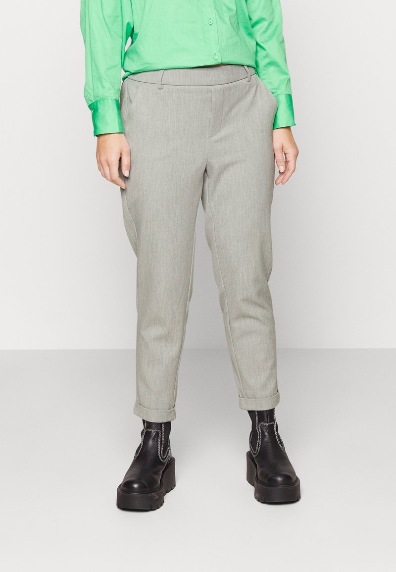 Personne portant un pantalon gris clair fuselé roulé aux chevilles, une chemise vert vif à manches longues, et des bottes à plateforme noires avec des coutures blanches.