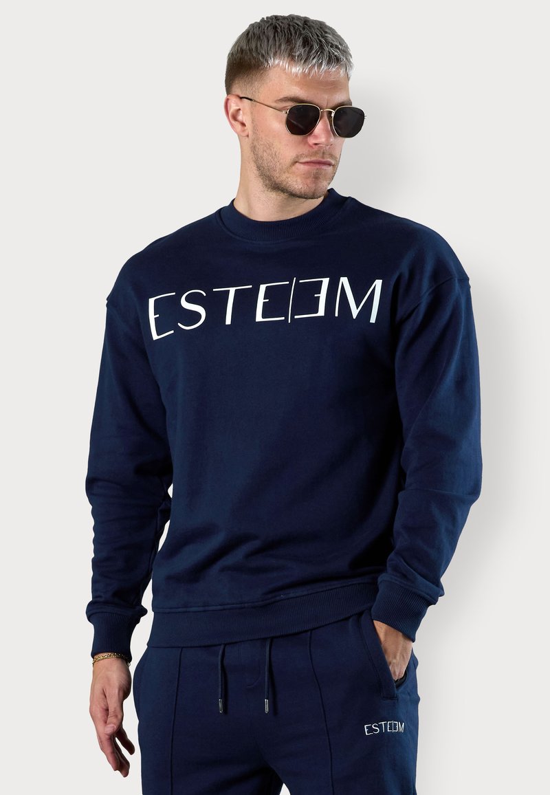Sweat-shirt bleu marine à col rond, arborant le texte blanc "ESTEEM" sur le devant. Fabriqué en tissu doux, il possède des poignets et un ourlet côtelés.