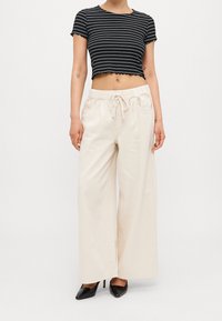 Camisa recortada a rayas en blanco y negro con dobladillo en forma de concha, combinada con pantalones de pierna ancha color crema con cintura ajustable y bolsillos laterales.