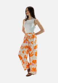 Witte mouwloze top gecombineerd met losse, elastische broek met een levendig oranje en roze bloemenpatroon en een wijde pijp.